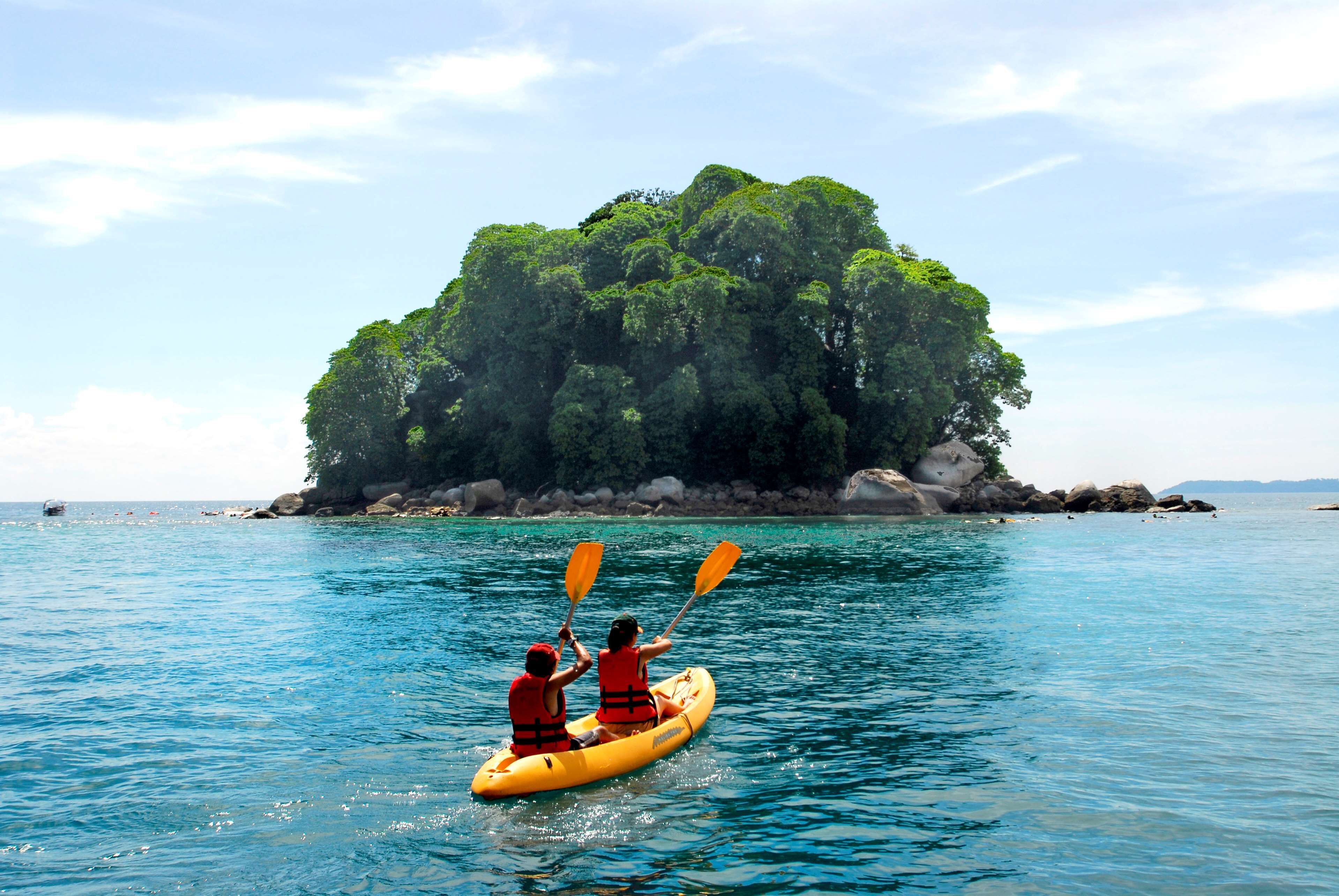 Two people kayaking on a calm sea with a small island in the background.