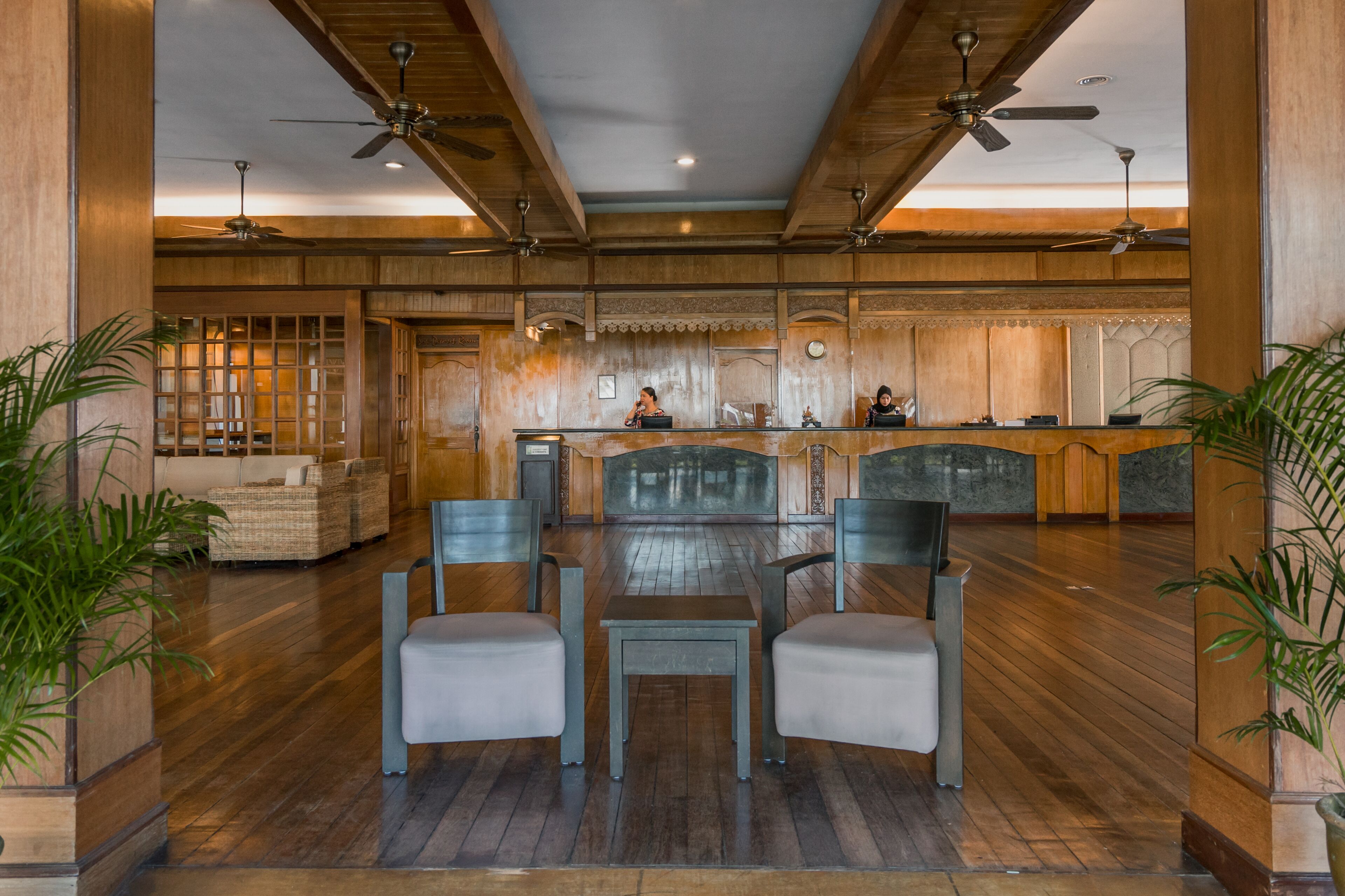 A spacious lobby with a wooden floor, a reception desk, and a seating area with two chairs and a table.