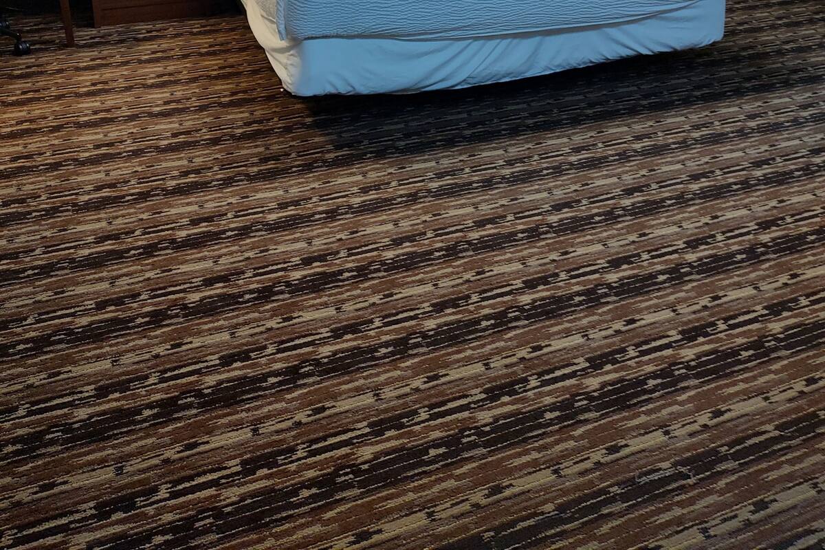 Een hotelkamer met een groot bed, twee nachtkastjes met lampen, een houten hoofdeinde en een groot schilderij van een zonsondergang aan de muur.