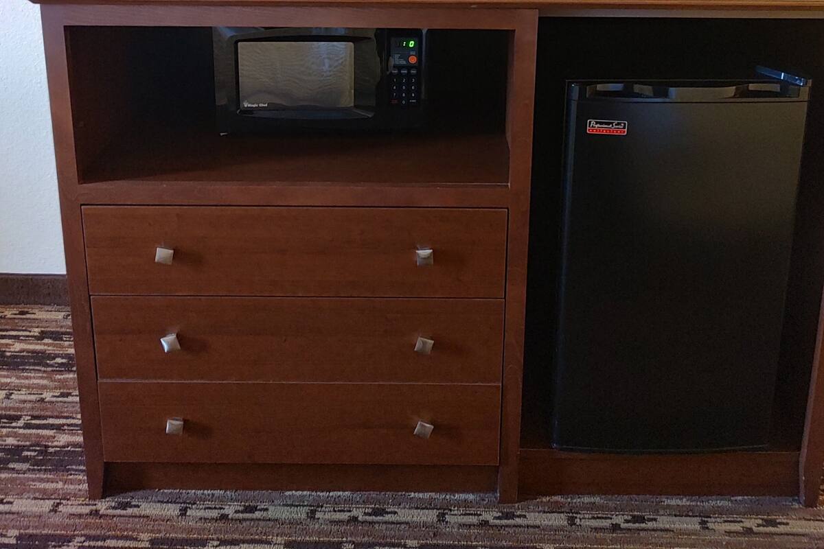 Een houten kast met een magnetron, koelkast en een flatscreen televisie die aan de muur is bevestigd.