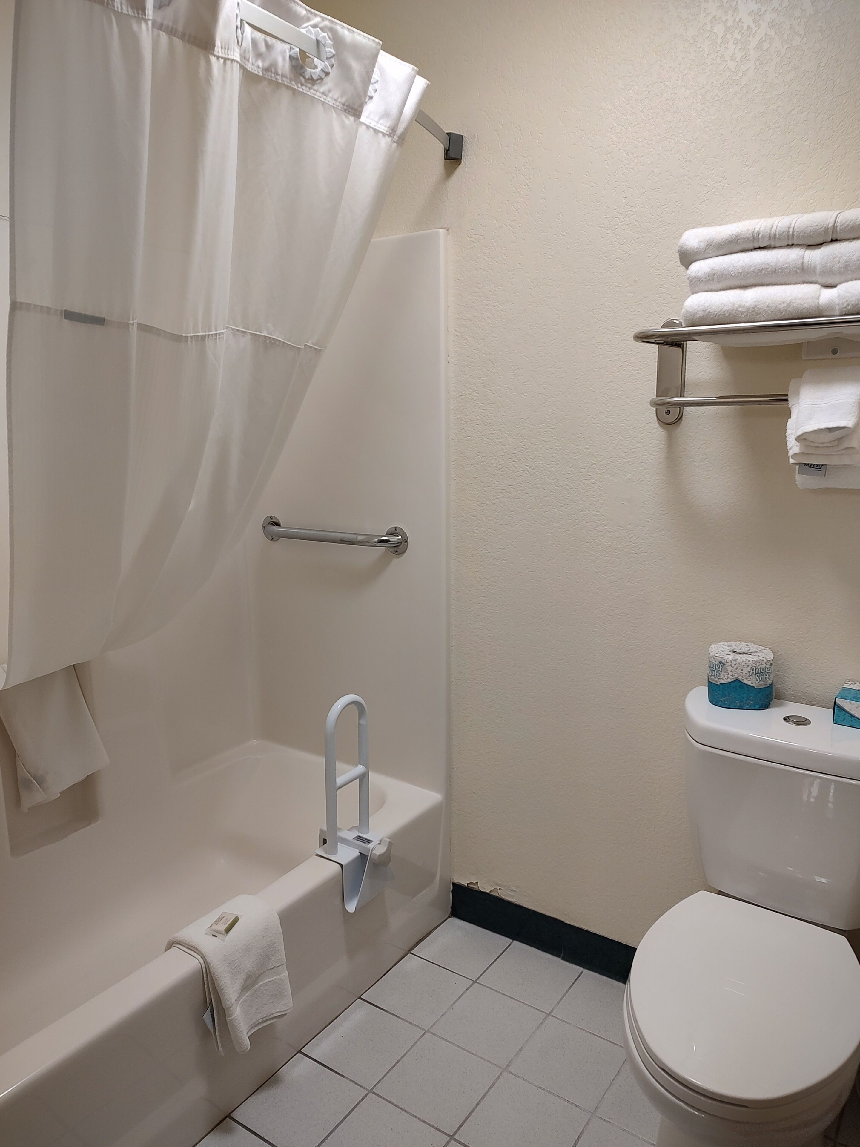A bathroom with a bathtub, a shower curtain, a toilet, and a towel rack.