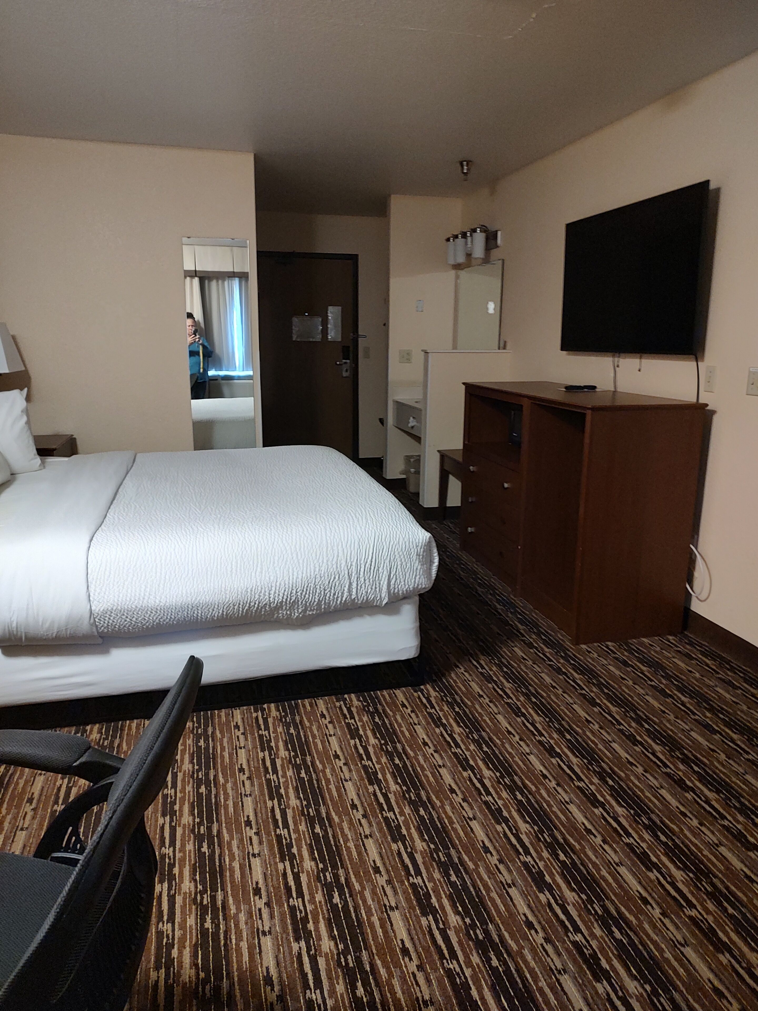 A hotel room with a bed, a desk, a chair, a TV, and a mirror.