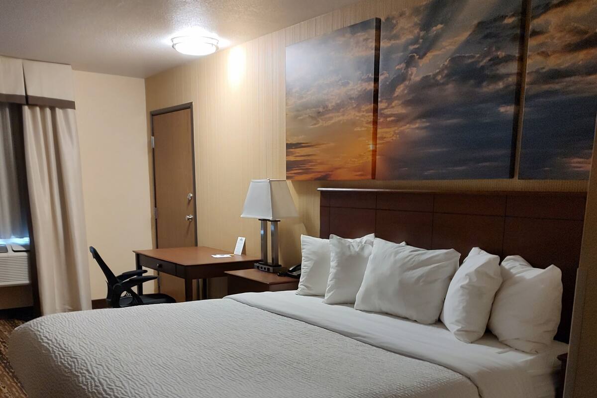 Een hotelkamer met een groot bed, een bureau, een stoel, een lamp en een schilderij van een zonsondergang aan de muur.