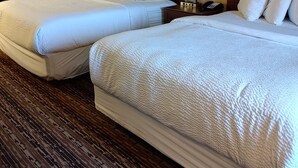 Une chambre d’hôtel avec deux lits, une table de chevet avec une lampe et un grand tableau représentant un paysage, placé au-dessus des lits.