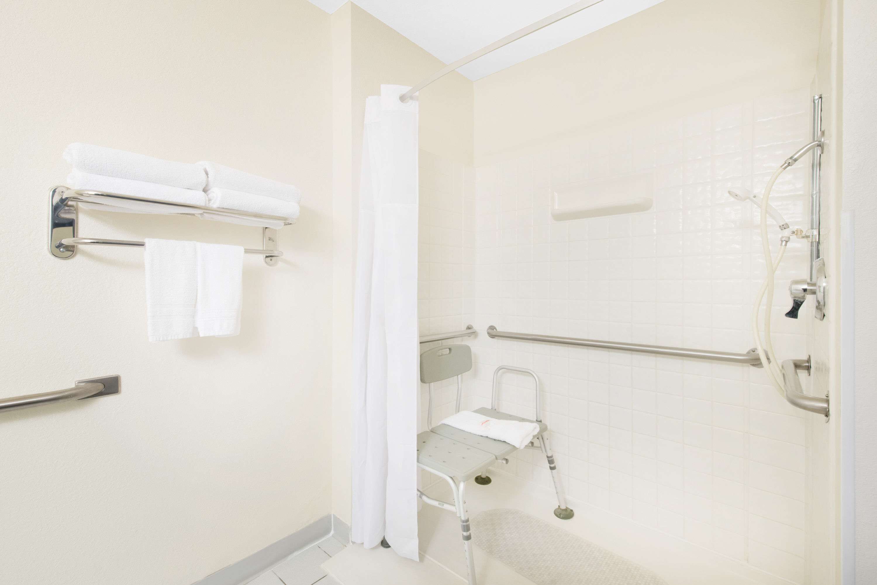 Une salle de bain équipée d’une douche, d’une barre d’appui, d’un banc accessible aux personnes en fauteuil roulant et d’un porte-serviettes.