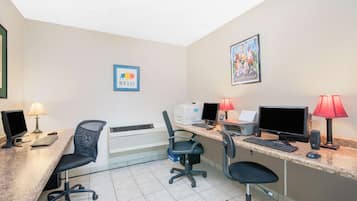 A hotel room with a desk, two chairs, two computers, a printer, and a wall-mounted air conditioner.