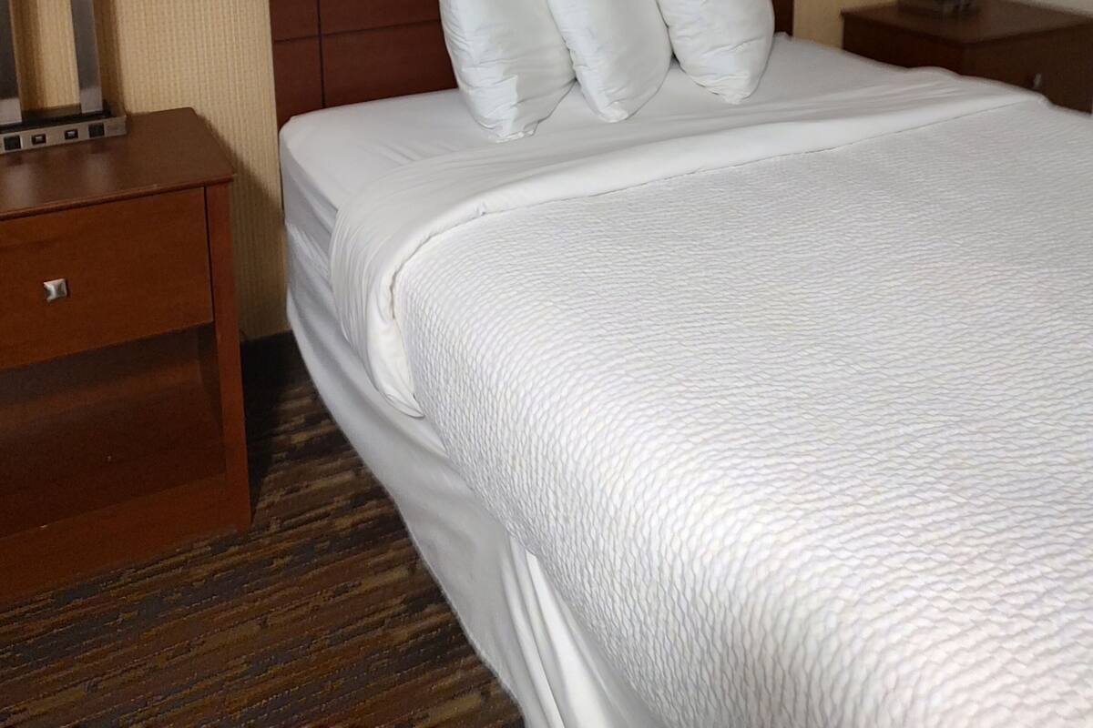 Een hotelkamer met een groot bed, een houten hoofdbord, twee nachtkastjes met lampen en een schilderij boven het bed.
