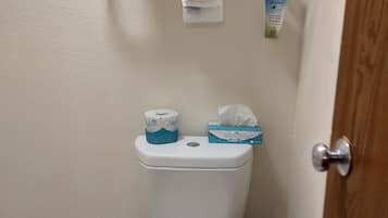 Une salle de bain comprenant des toilettes, un porte-serviettes avec des serviettes pliées, du papier toilette et une poubelle.