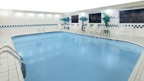 Une grande piscine intérieure à l’eau d’un bleu limpide, entourée de chaises blanches et de plantes en pot.