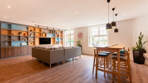Una sala moderna con un sofá gris, suelo de madera, estanterías empotradas, un televisor de pantalla plana y un comedor con sillas y una mesa de madera.