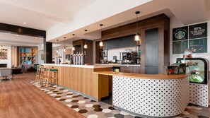 A modern bar area with a wooden counter, bar stools, and a coffee machine. - Holiday Inn Darlington - A1 Scotch Corner by IHG (Richmond)