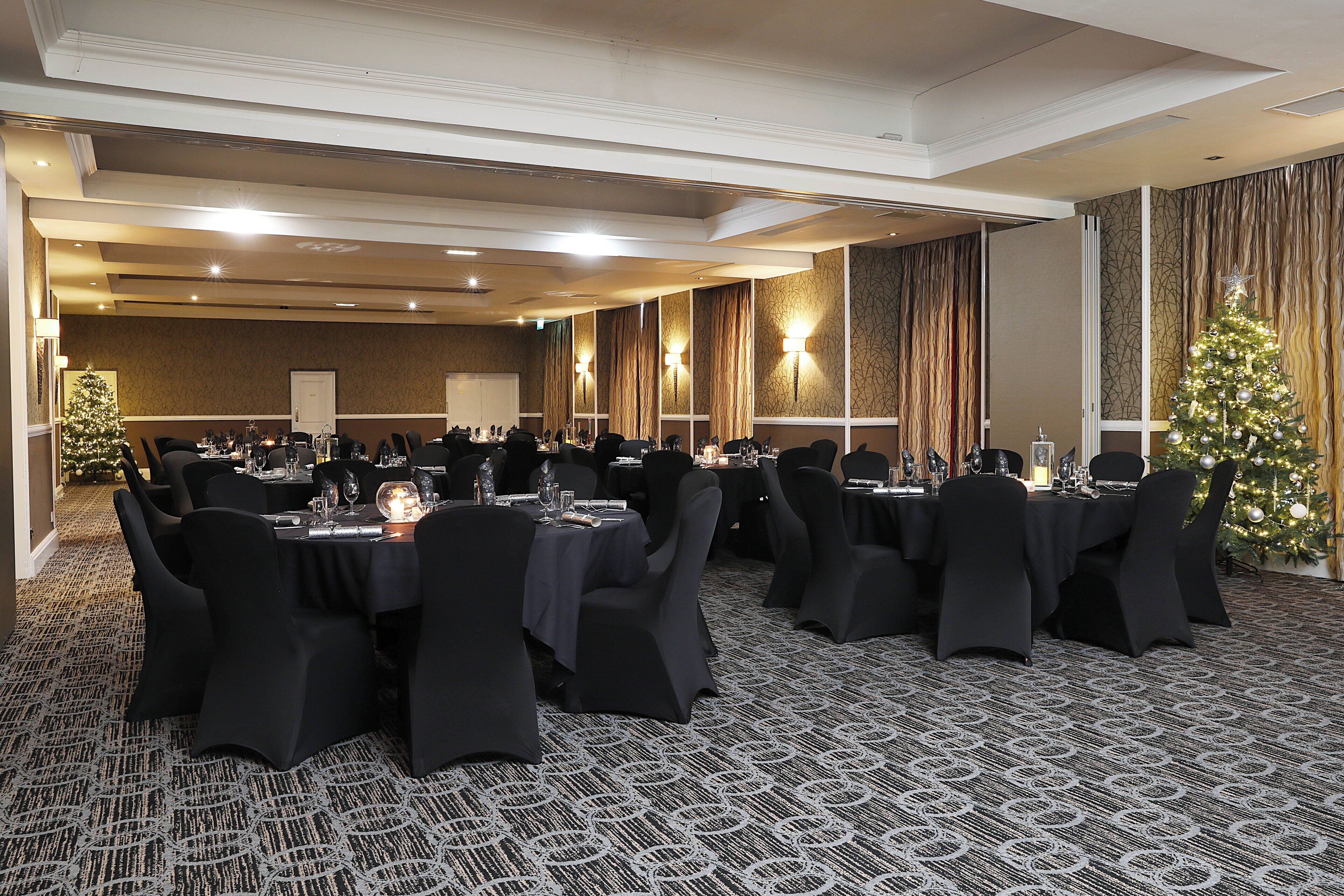 A conference room with tables set for a meeting, equipped with chairs and tables, and a Christmas tree in the corner.
