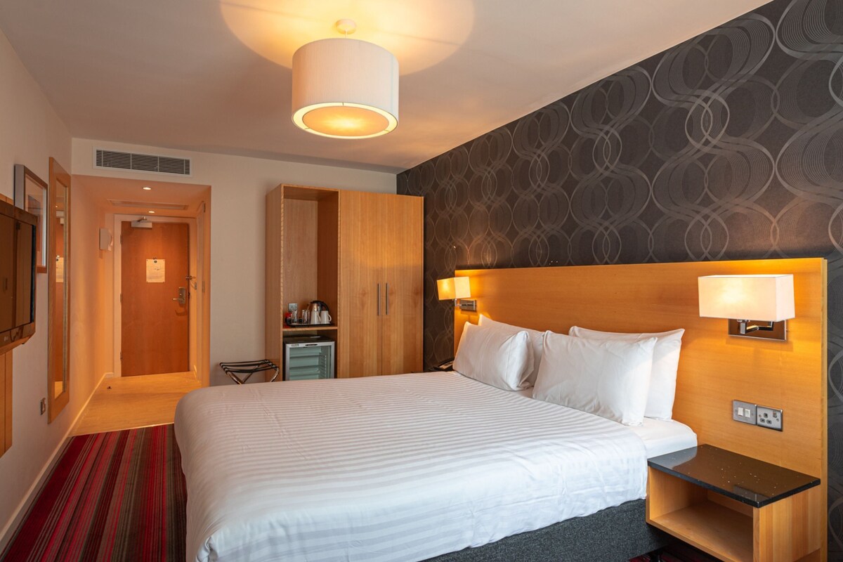 A hotel room with a large bed, bedside lamps, a flat-screen TV, a desk, and a wardrobe.