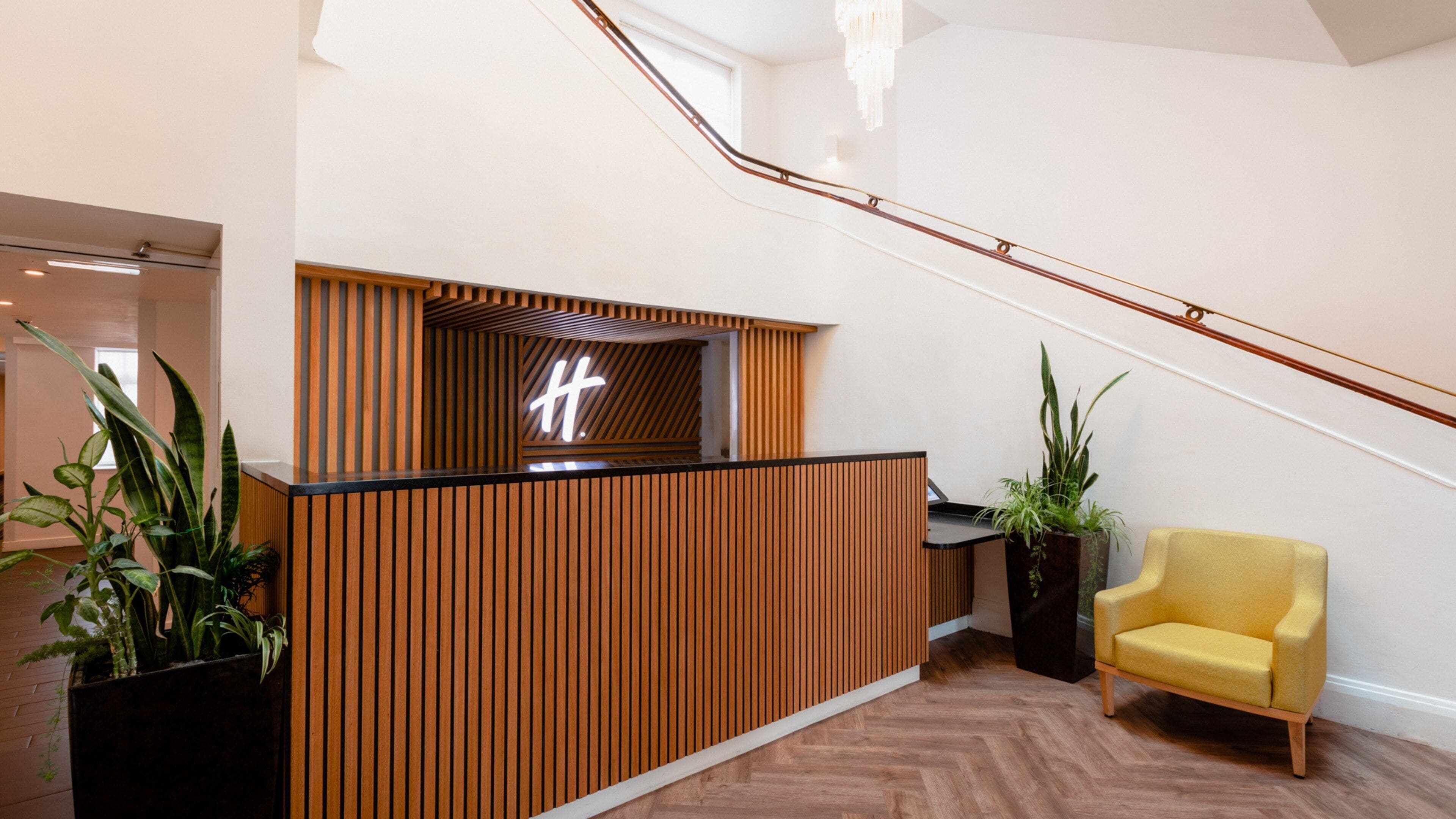 Una recepción con diseño de listones de madera, un sillón amarillo y una escalera.