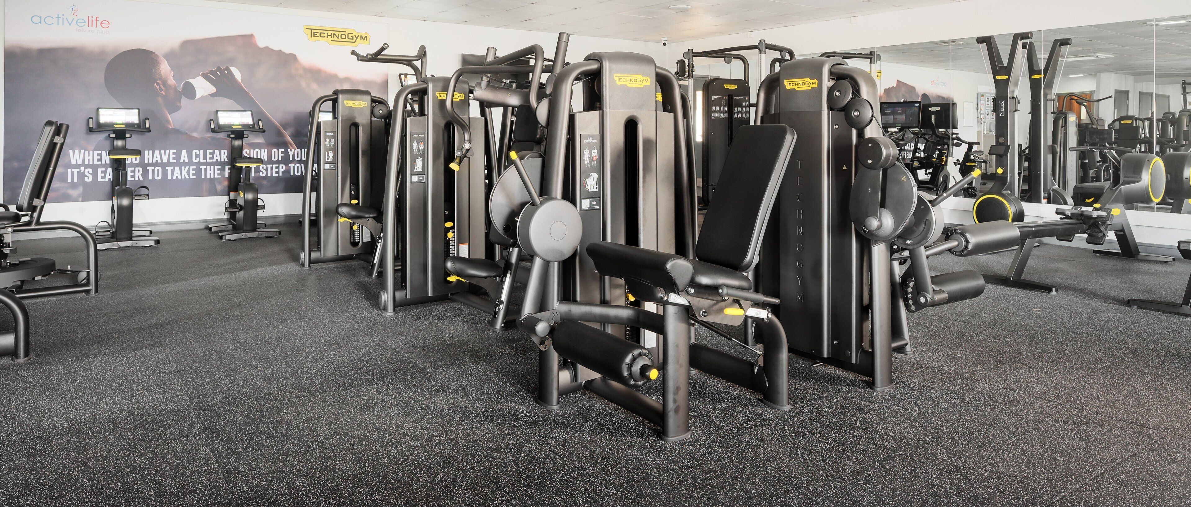 Un gimnasio con diversas máquinas de ejercicio, espejos y carteles motivacionales.