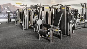 Un gimnasio con diversas máquinas de ejercicio, espejos y carteles motivacionales.