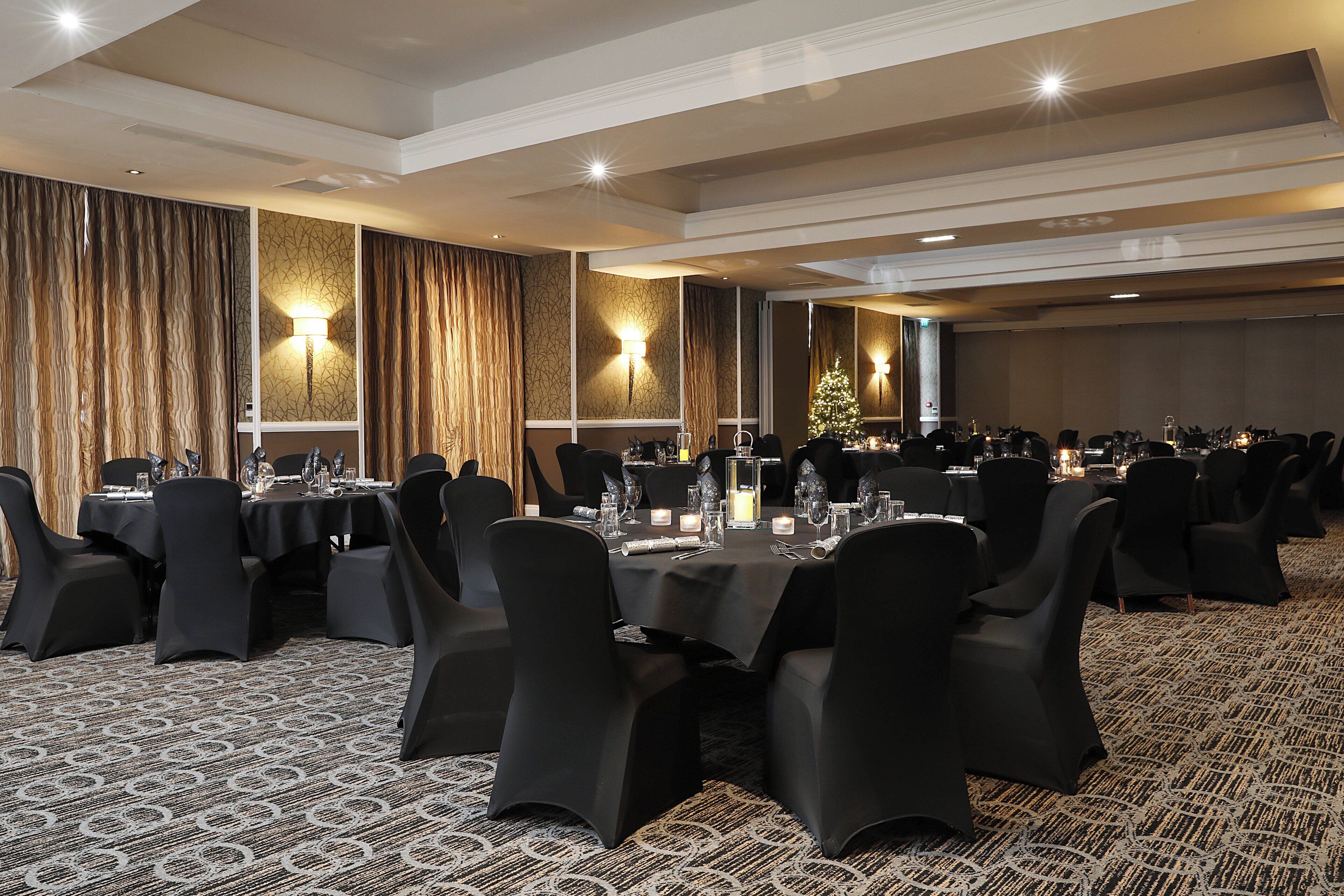 A banquet hall with round tables, black chairs, and a patterned carpet.