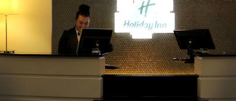 En receptionsdisk på ett Holiday Inn-hotell, med en vägg som har en intressant yta och en stor, upplyst skylt.