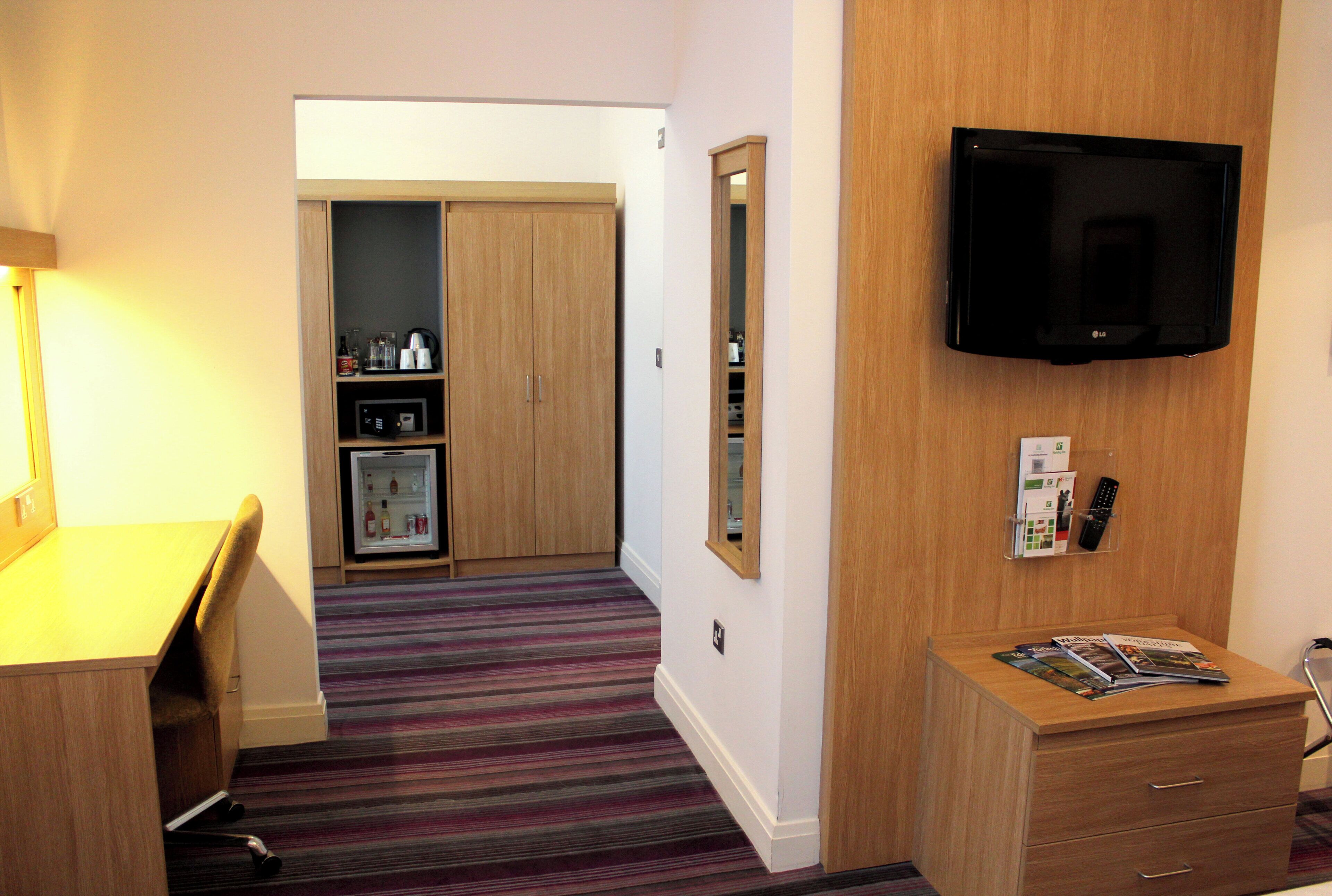 A hotel room with a bed, a desk, a television, a refrigerator, and a bathroom.
