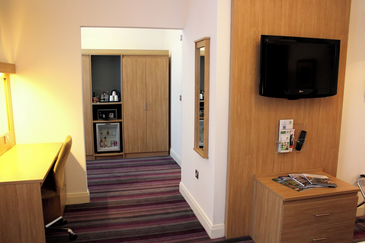 A hotel room with a bed, a desk, a television, a refrigerator, and a bathroom.