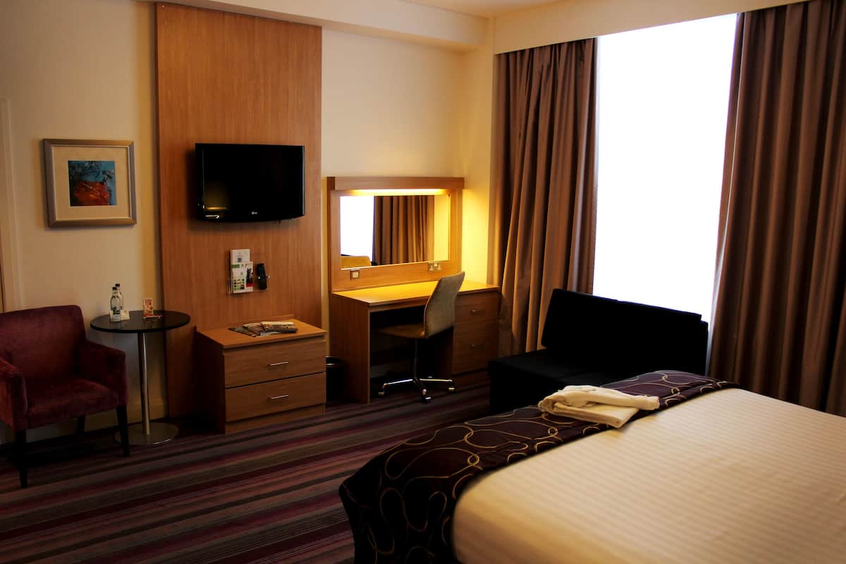 A hotel room with a bed, a desk, a chair, a television, and a window with curtains.