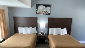 A hotel room with two beds, a nightstand with a lamp, and a painting of flowers on the wall. - Paso Robles Travelodge (Paso Robles)