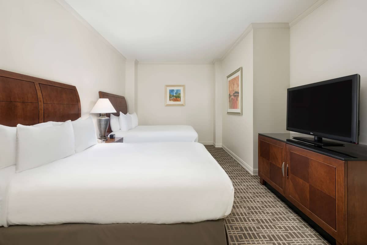 A hotel room with two beds, a TV, a lamp, and a cabinet.
