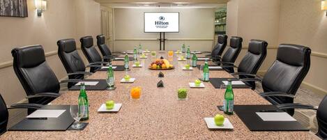 A conference room with a long table, black leather chairs, and a screen displaying the Hilton logo.