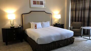 Habitación de hotel con una cama grande, dos lámparas de noche, un cuadro en la pared, una silla y una mesita.