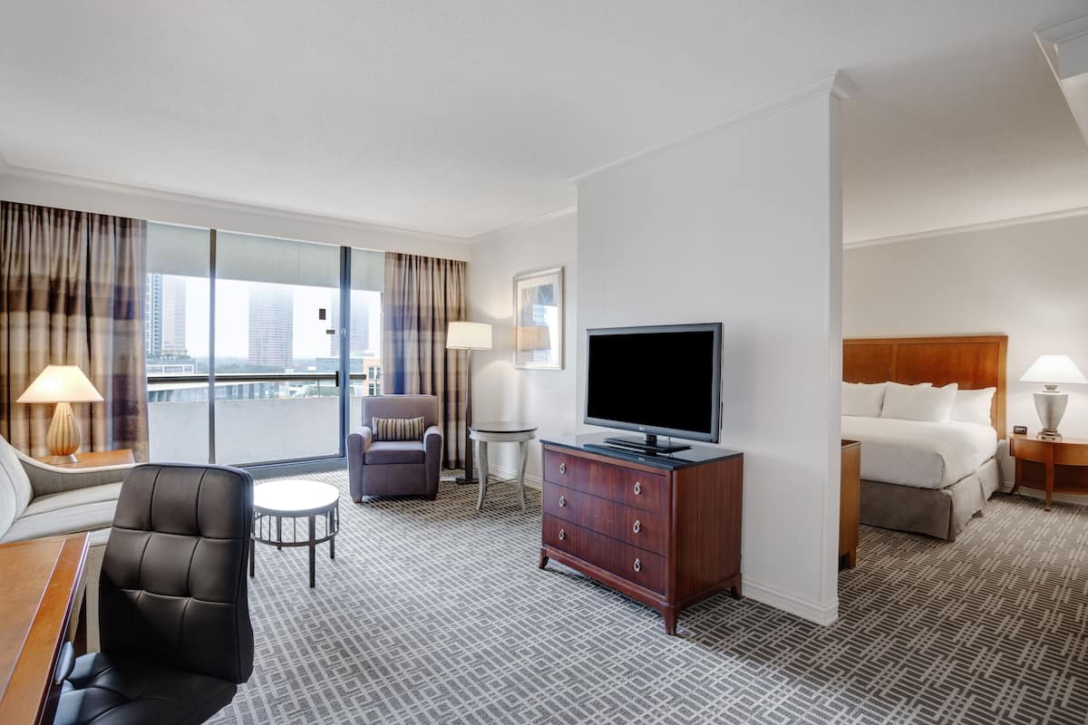 A hotel room with a large window, a flat-screen TV, a bed, a desk, a chair, and a dresser.
