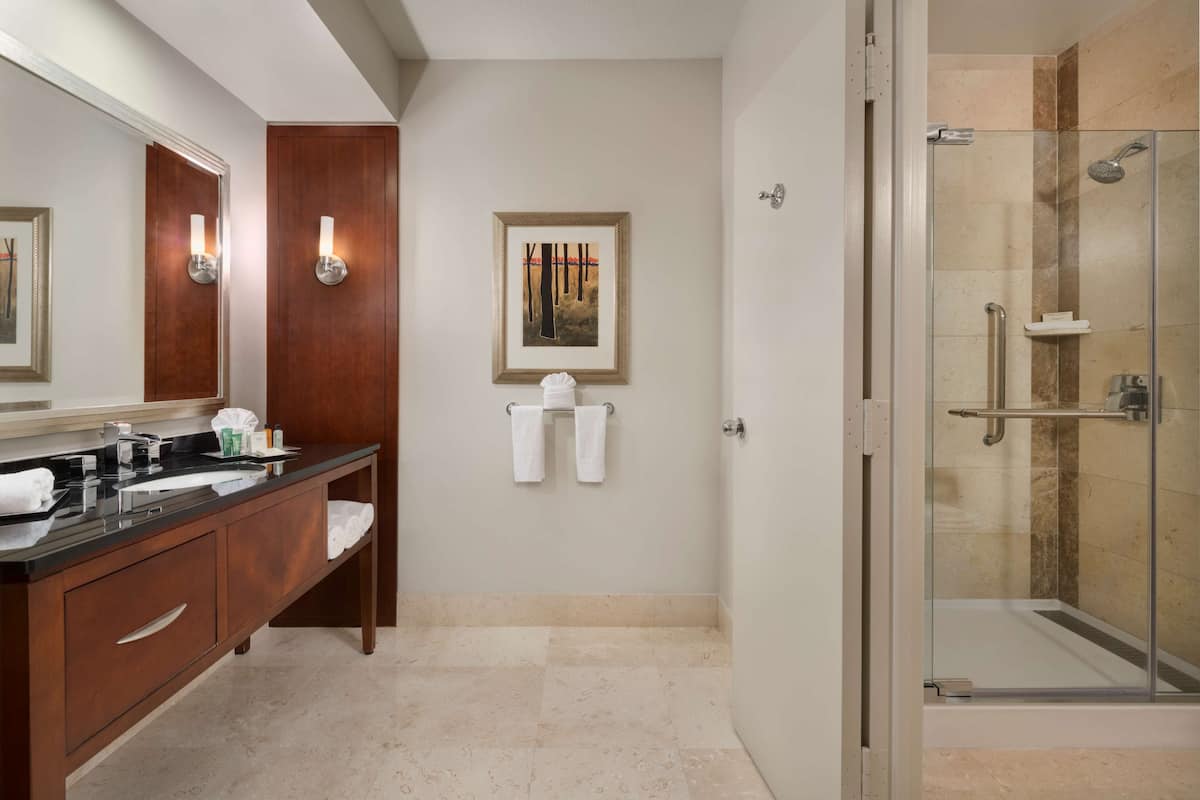 A modern bathroom with a glass-enclosed shower, a wooden vanity with a black countertop, and a framed picture on the wall.
