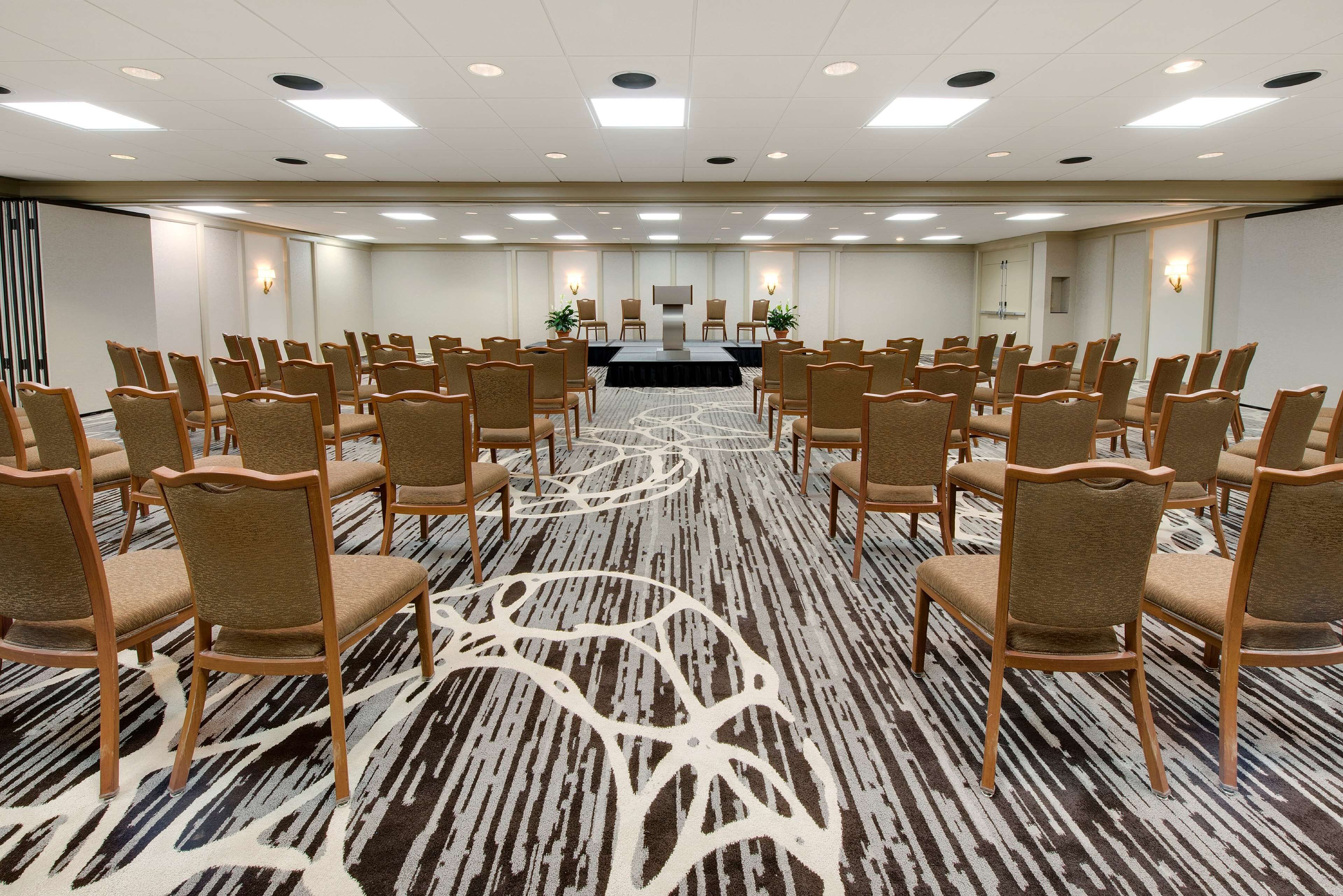 A conference room with rows of chairs, a stage, and a carpeted floor.