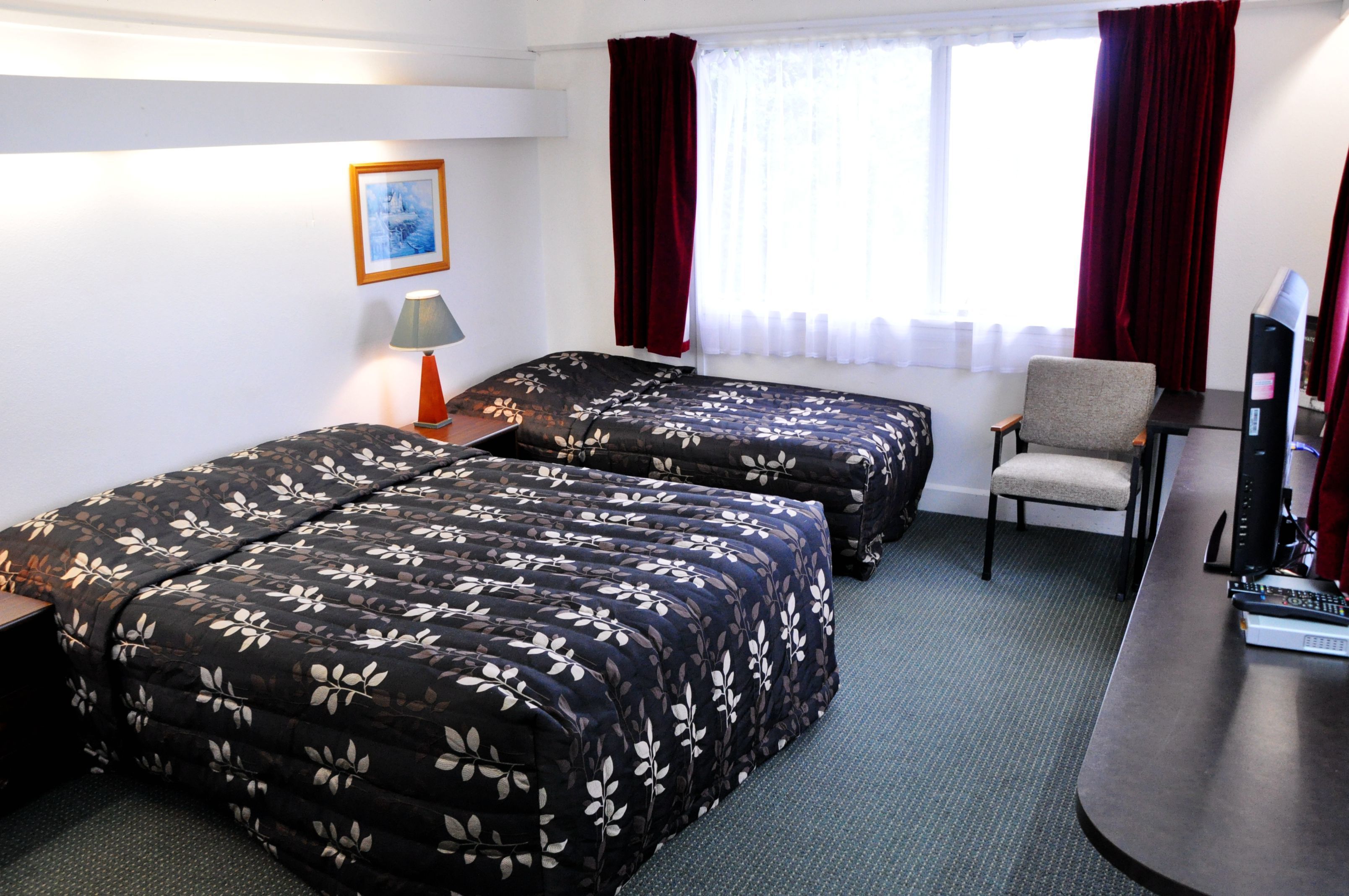 Habitación de hotel con dos camas, un escritorio, una silla, un televisor y una ventana con cortinas.