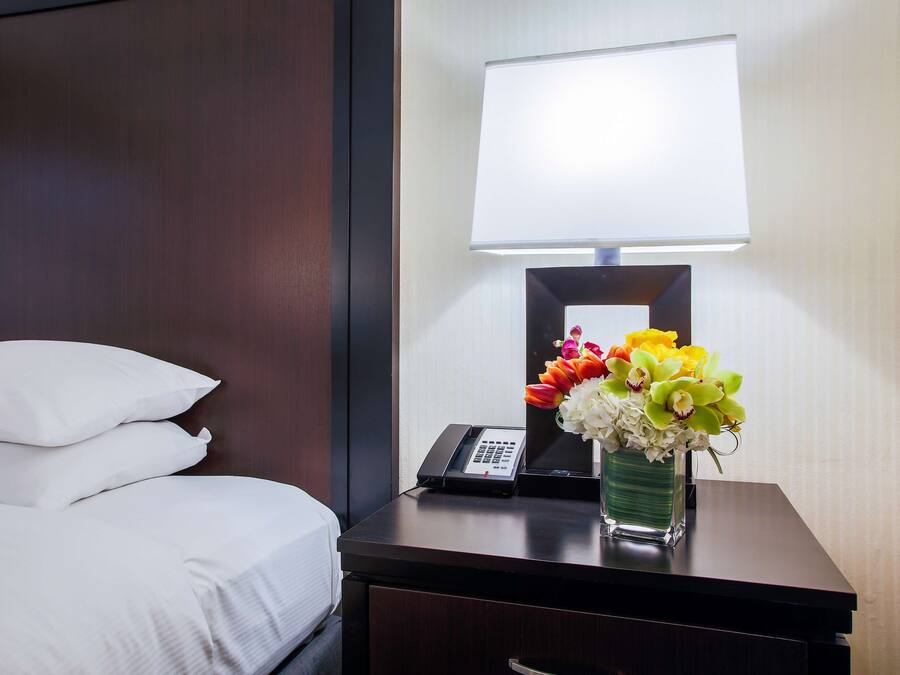 Ein Hotelzimmer mit Bett, Nachttisch mit Lampe, Telefon und Blumen in einer Vase.