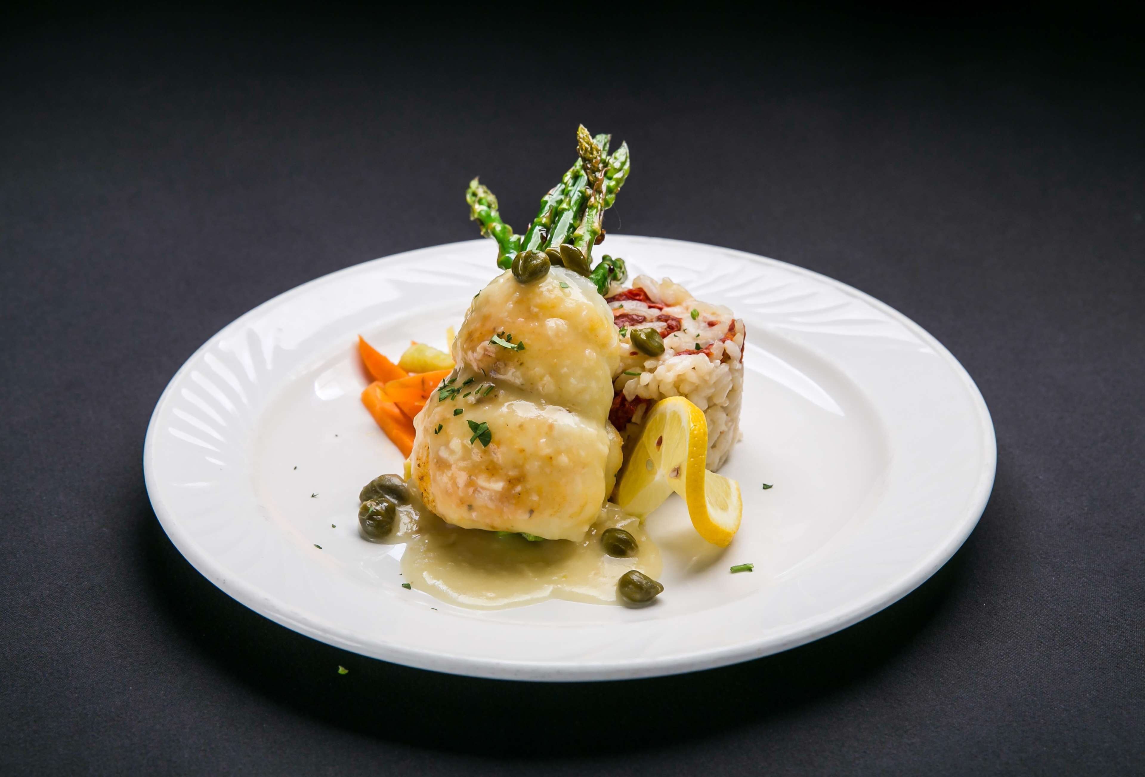 Um prato branco com uma porção de comida, incluindo um hambúrguer, um bolinho e alguns vegetais.