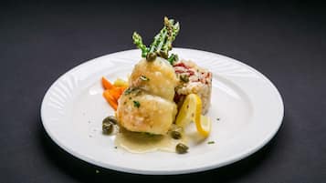 Um prato branco com uma porção de comida, incluindo um hambúrguer, um bolinho e alguns vegetais.