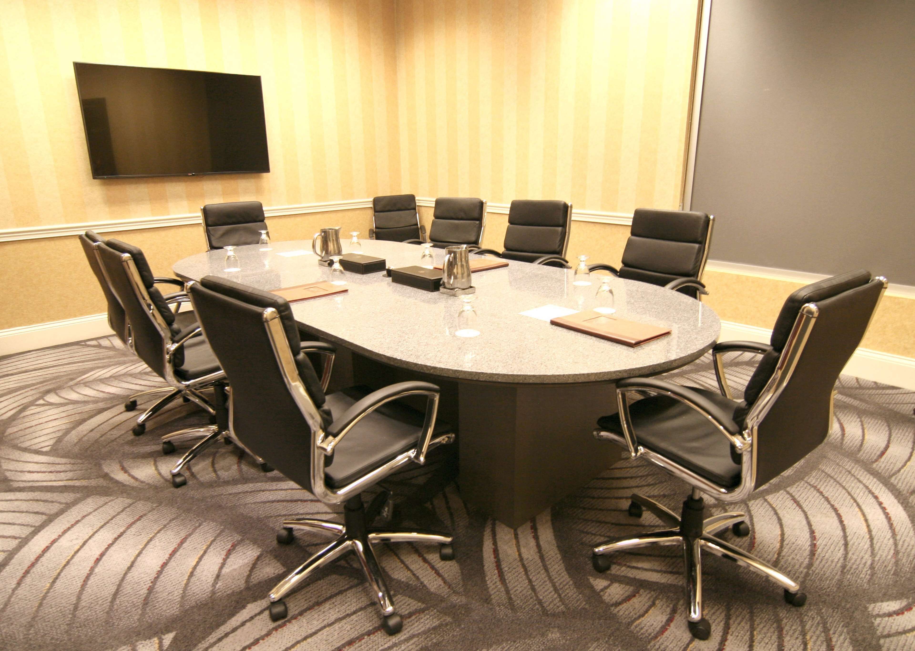 A conference room with a large table, eight chairs, a flat-screen TV, and a carpeted floor.