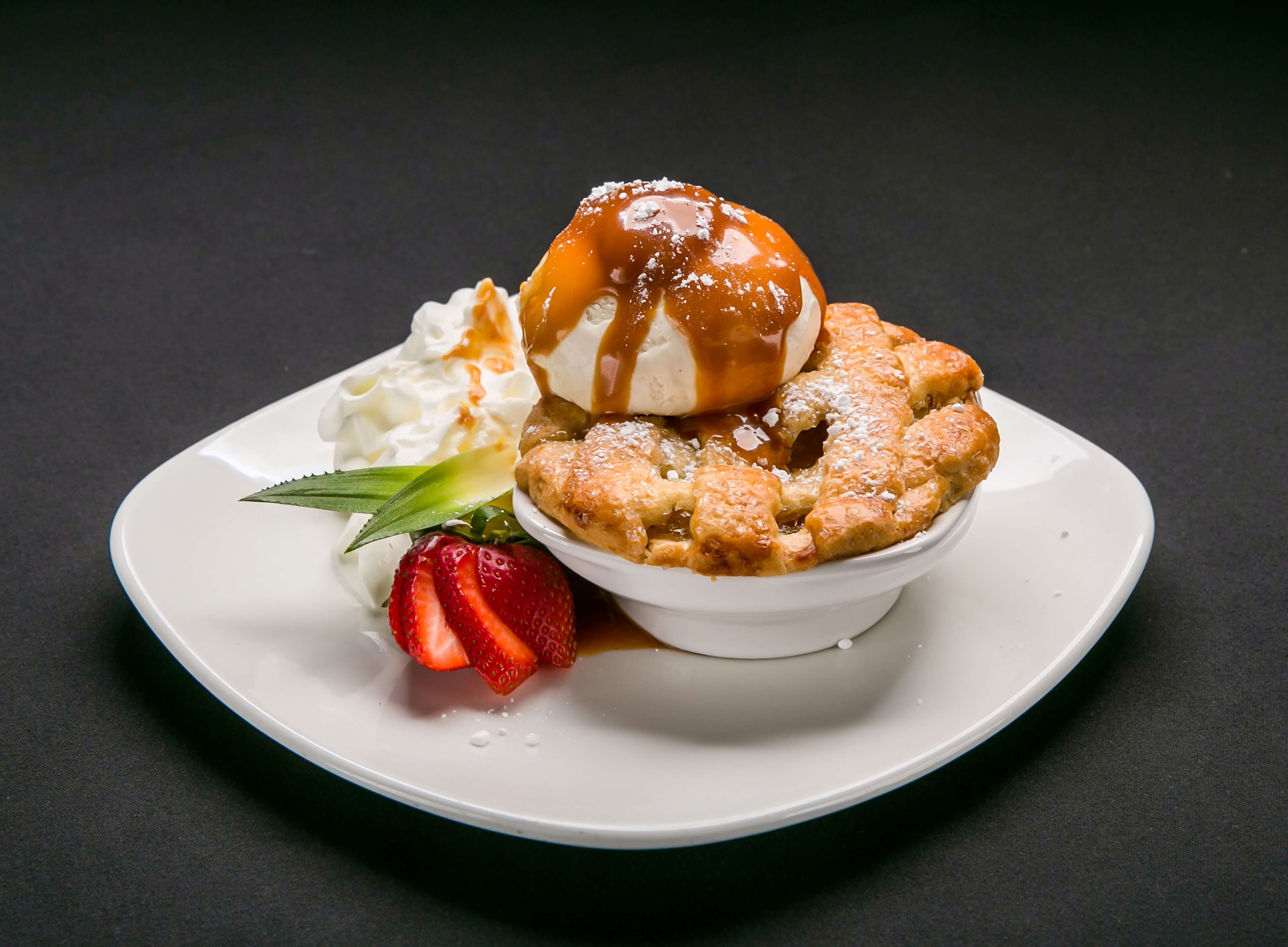 Un plato de postre con una bola de helado, una porción de pastel, crema batida y una fresa.
