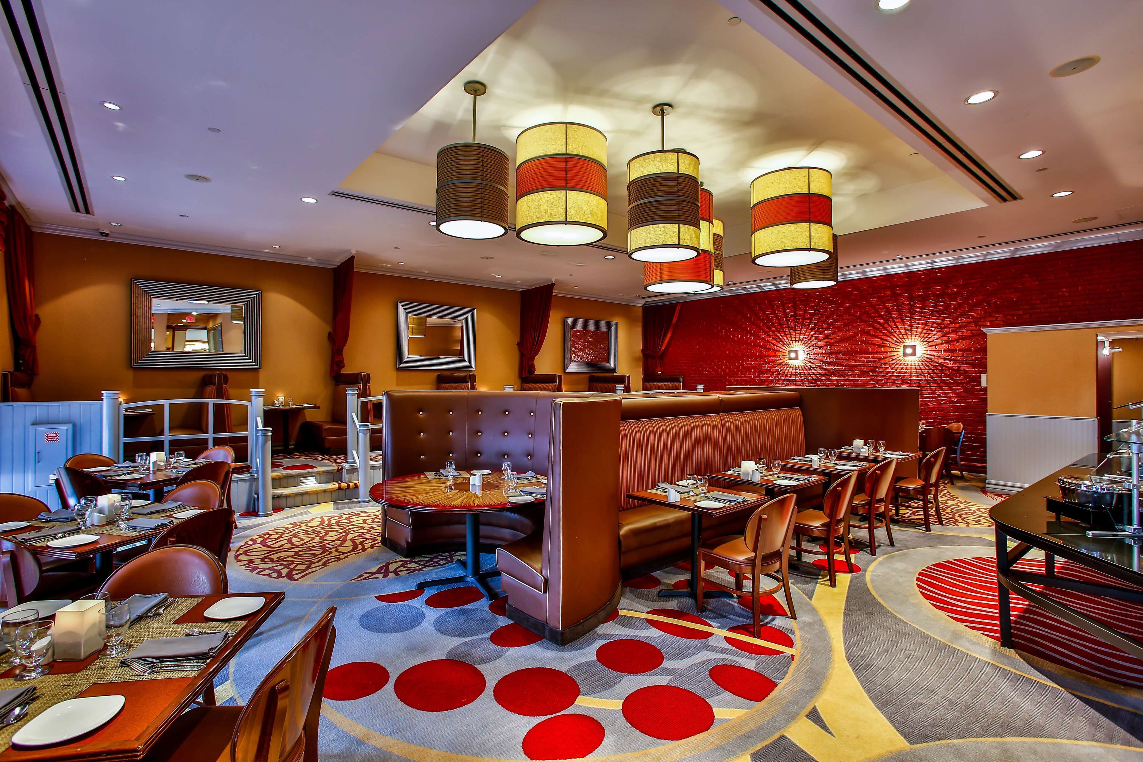 Een restaurant met zitplaatsen in hokjes, ronde tafels en een kamerbreed tapijt met patroon.