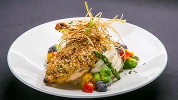 A white plate with a piece of breaded fish, asparagus, and colorful vegetables.