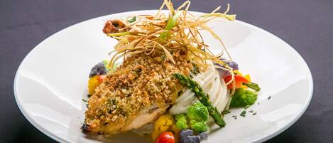 Une assiette blanche contenant un morceau de poisson pané, des asperges et des légumes de différentes couleurs.