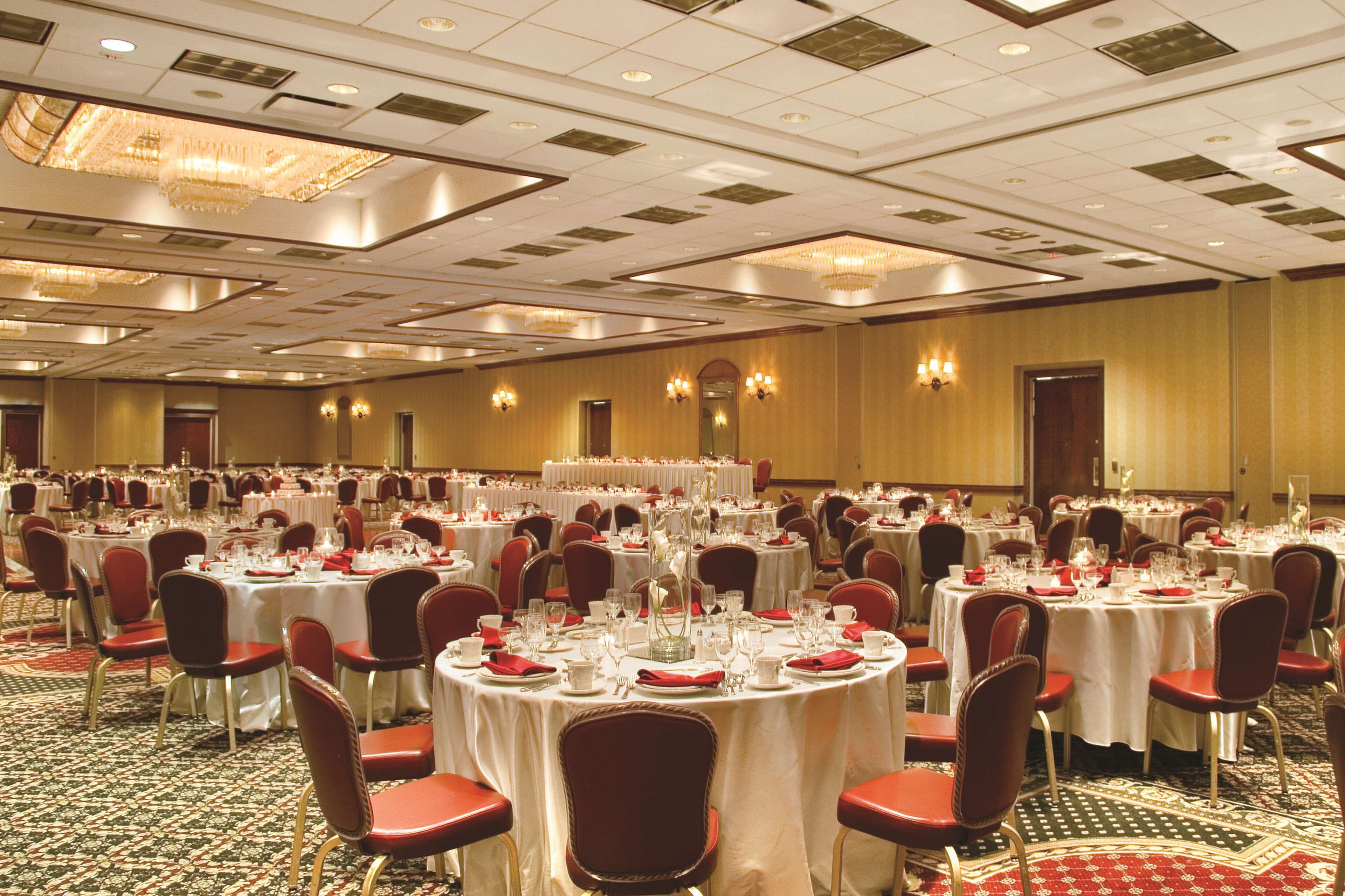 Un gran salón de banquetes con varias mesas redondas dispuestas para comer, cada una con manteles blancos y sillas rojas.