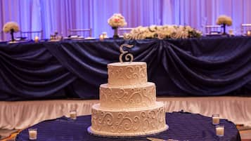 A three-tiered wedding cake with intricate icing designs on a table covered with a dark cloth.
