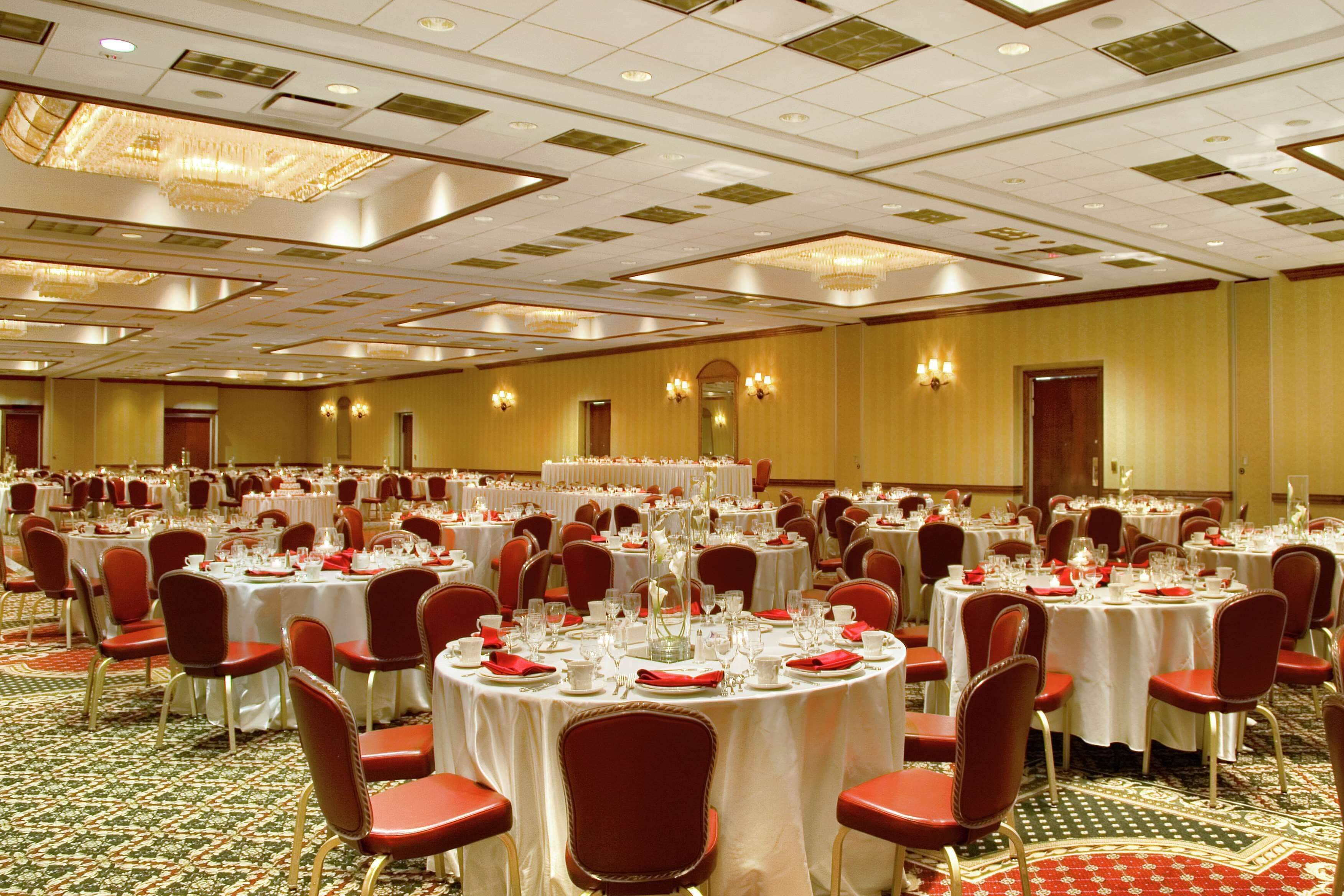 A banquet hall with round tables set for dining, red chairs, and chandeliers on the ceiling.