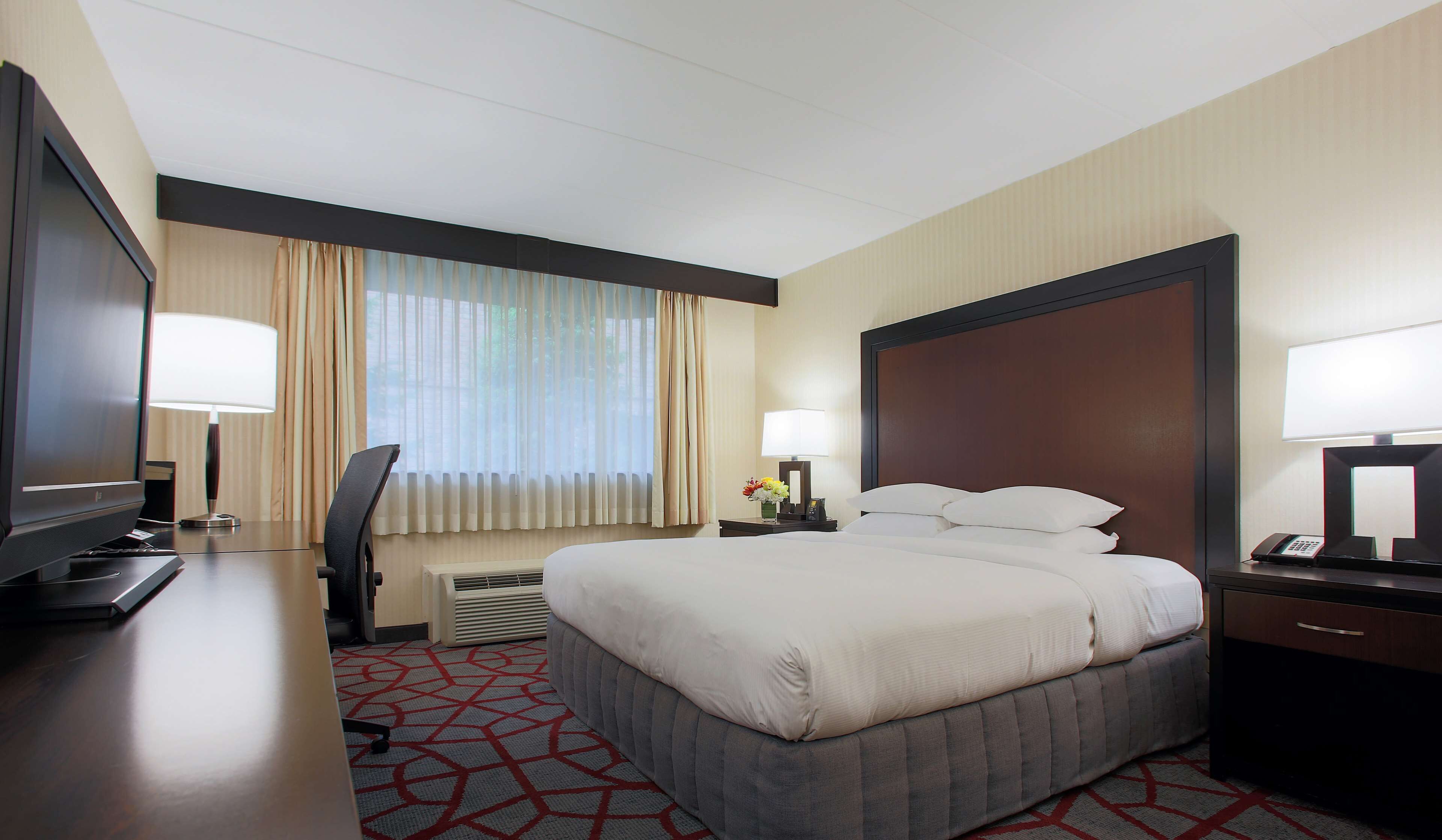 Une chambre d’hôtel avec un grand lit, un bureau avec un ordinateur, une télévision et un téléphone.