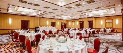 A large banquet hall with round tables set for dining, red upholstered chairs, and a carpeted floor.