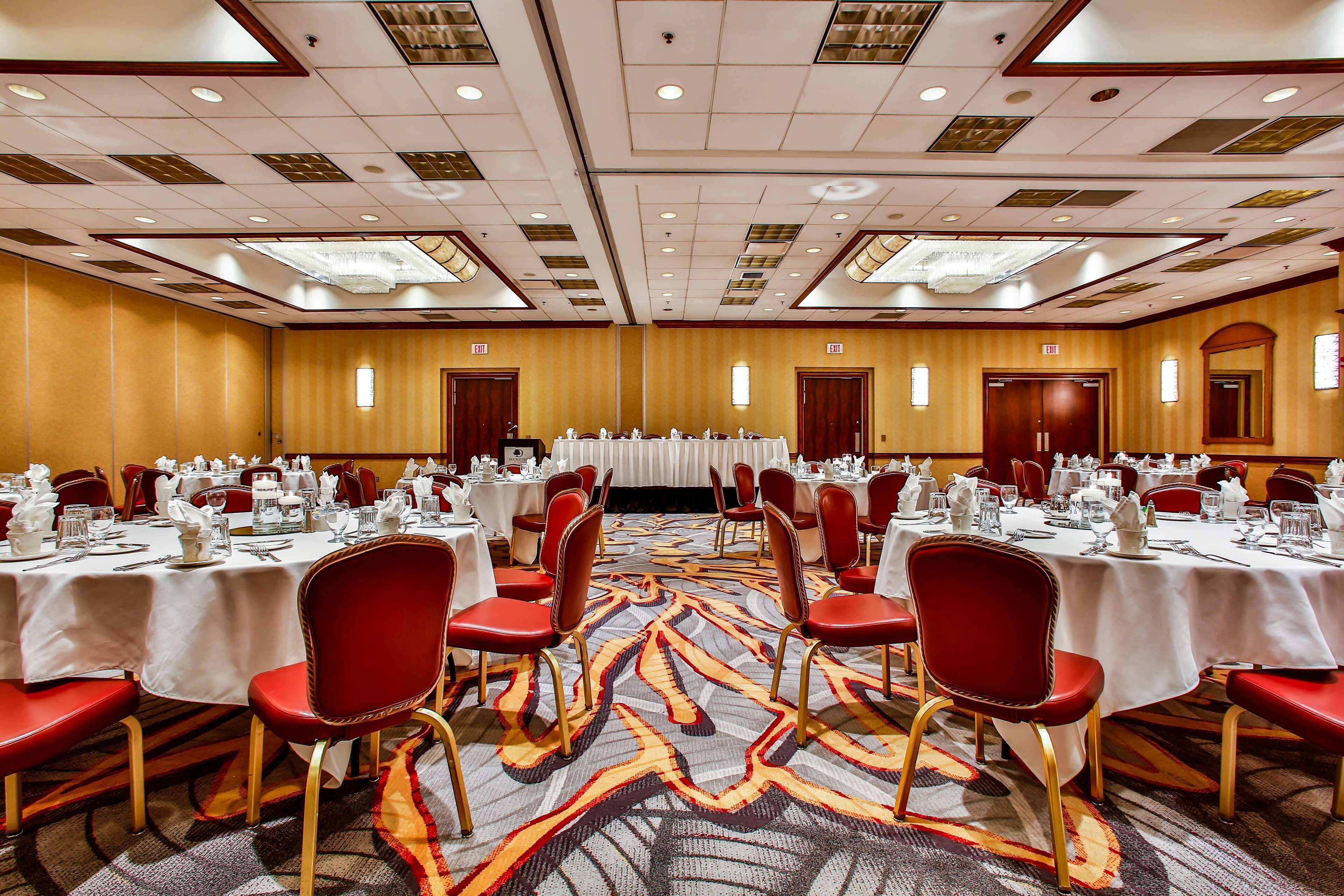 A banquet hall with round tables, red chairs, and a patterned carpet.