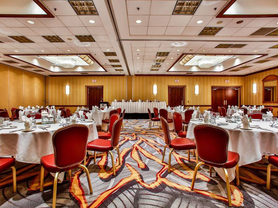 Une salle de banquet avec des tables rondes, des chaises rouges et un tapis à motifs.