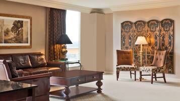 A living room with a brown leather sofa, a wooden coffee table, and two patterned armchairs. A large framed painting is on the wall, and a decorative screen is behind the armchairs.