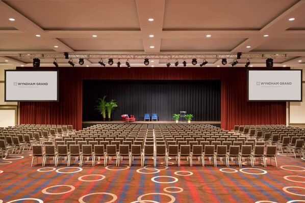 A conference room with rows of chairs, a stage with a screen, and a carpet with circular patterns.